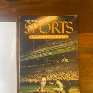 Może przedstawiać: Okładka vintage magazynu Sports Illustrated, pierwszy numer, z datą 16 sierpnia 1954. Na okładce przedstawiono trwającą grę w baseball, z graczem w czerwonym stroju uderzającym, graczem w białym stroju łapiącym i sędzią stojącym między nimi. Stadion jest pełen widzów.