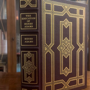 May include: A burgundy leather-bound book with gold accents and the title "The Education of Henry Adams" on the spine. The book is by Henry Adams.