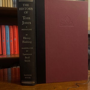 May include: A burgundy hardcover book with a black spine. The book title is "The History of Tom Jones, A Foundling" by Henry Fielding. The book is illustrated by Lawrence Beall Smith and published by Random House.