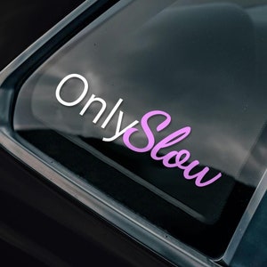 May include: A black car with a pink and white sticker on the rear window that says "Only Slow". There is a black and white sticker on the side of the car that says "Bad Investments Auto 2016".