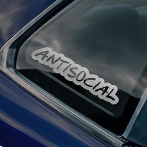 May include: A blue car with a sticker on the rear window that says "ANTISOCIAL". There is another sticker on the side of the car that says "BAD INVESTMENTS AUTO 2016" with a stylized "A" in the center.