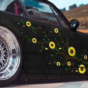 May include: Black car with a sunflower decal design. The decal features yellow sunflowers, green leaves, and brown branches. The car has a silver wheel and the text "EXCLUSIVE PRODUCT & DESIGN OF INVESTMENTS AUTO CLUB".
