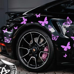 May include: Black sports car decorated with multiple purple butterfly decals. The car has black rims and a sticker that says "BAD INVESTMENTS AUTO" with the year 2016.