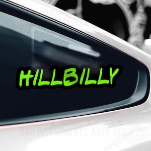 May include: A black car window with a green "HILLBILLY" decal. The decal is in a bold, handwritten style.