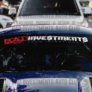 May include: A black car with a white and red decal that reads "BAD INVESTMENTS GOOD INTENTIONS" on the windscreen. The decal is an exclusive product and design of BAD INVESTMENTS AUTO CLUB.