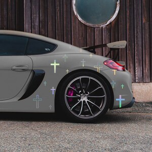 May include: A grey sports car with a black spoiler and black wheels. The car has a variety of iridescent cross decals on the side.