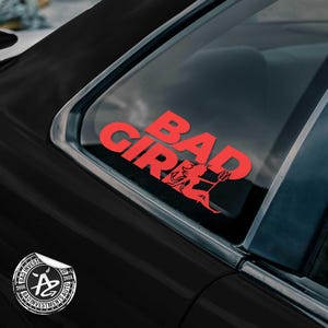 May include: Red "BAD GIRL" decal with a devil graphic on a car window. The sticker is on a black car. A circular sticker with the text "BAD INVESTMENTS AUTO" is also visible.