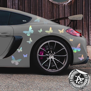 May include: A grey sports car with iridescent butterfly decals on the side and rear. The car has a black spoiler and black wheels. The car is parked in front of a wooden fence. The car has a sticker on the rear bumper that says "Bad Investments Auto 2016".