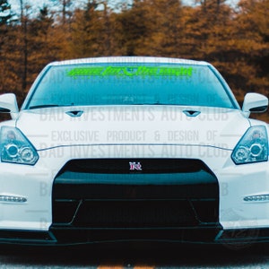 May include: A white car with a black front bumper and a green and white decal on the windshield that reads "Game For The Win Making Memories".