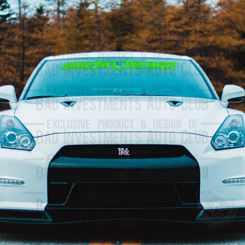 May include: A white car with a black front bumper and a green and white decal on the windshield that reads "Game For The Win Making Memories".