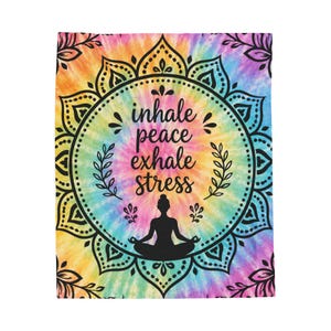 May include: A rectangular blanket featuring a vibrant rainbow tie-dye background. Centered is a black mandala design with a silhouette of a person in a seated meditation pose. The text reads: inhale, peace, exhale, stress in black script.