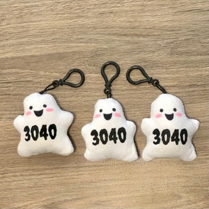 May include: Three white plush ghost keychains with black eyes and mouths, pink cheeks, and the number 3040 printed on each. The ghosts are attached to black metal key rings.