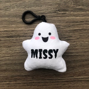 May include: White plush ghost keychain with a black clip, pink cheeks, a smiling face, and the name "MISSY" in black text.