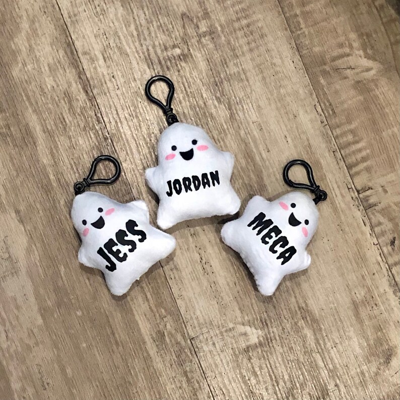 May include: Three white plush ghost keychains with black eyes and mouths. Each ghost has a different name written on it: Jess, Jordan, and Mecca.