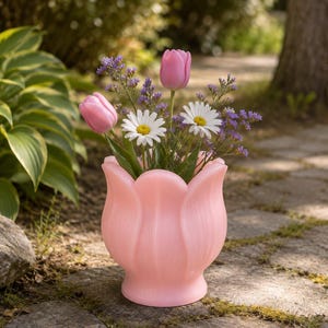 May include: A light pink tulip-shaped vase holding a bouquet of two pink tulips, two white daisies with yellow centers, and sprigs of small purple flowers. The vase features a molded petal design with a smooth, rounded base and a flared rim.