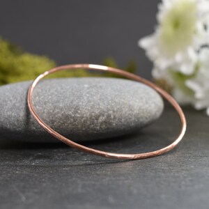May include: A simple, hammered copper bangle bracelet. The bracelet is a solid, smooth circle with a slightly textured surface.