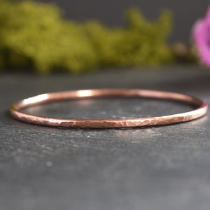 May include: A hammered rose gold bangle bracelet. The bracelet is thin and delicate, with a smooth, polished finish.