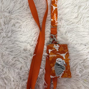 May include: Orange lanyard and matching dog waste bag holder. The lanyard features the text "Longhorns" and a Longhorn logo. The dog waste bag holder has a Longhorn logo and the text "Dog Years Fashion".