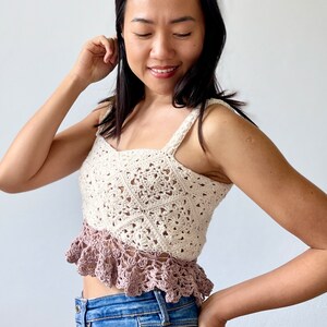 May include: A crocheted tank top with a white top and a pink bottom. The top is made with a delicate stitch pattern and the bottom has a ruffled edge.
