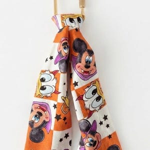 May include: A fabric ribbon featuring a repeating pattern of cartoon characters dressed as vampires, including Mickey Mouse and Donald Duck, set against an orange and white checkered background with small black stars, attached to a gold metal U-shaped clasp.