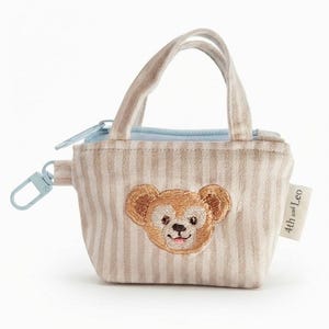May include: A small beige and white striped fabric pouch shaped like a tote bag with two handles. It features an embroidered bear face on the front, a light blue zipper closure, and a light blue plastic clip. A white tag reads 4th and Leo.