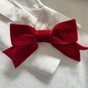 May include: A close-up of a red velvet bow tie on a white dress shirt. The bow tie is a deep red color and has a soft, velvety texture. The white shirt has a crisp, clean appearance.