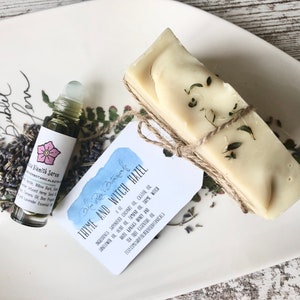 May include: A small bottle of serum with a pink flower graphic and the text "Blemish Serum" and a bar of soap wrapped in twine with a tag that reads "Blue Moon Botanicals Thyme and Witch Hazel" with a list of ingredients.