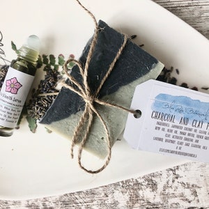May include: A white ceramic plate with a bar of charcoal and clay face soap tied with twine, a small glass bottle of blemish serum, and dried lavender flowers. The soap label reads "Blue River Botanicals Charcoal and Clay Face".