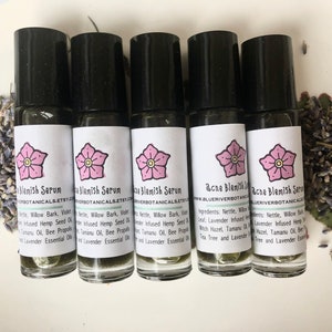May include: Five small glass bottles with black roll-on tops and white labels. The labels have a pink flower graphic and the text "Acne Blemish Serum" with the website address "www.blueriverbotanicals.etsy.com". The bottles are on a white surface with dried lavender flowers scattered around them.
