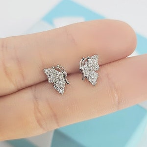 Puede incluir: Un par de pendientes de mariposa plateados con piedras de circonita cúbica transparentes.