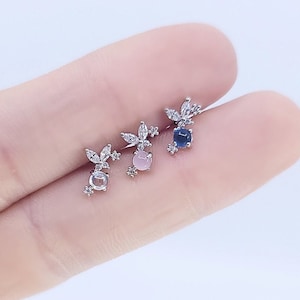 May include: Three silver butterfly earrings with different colored gemstones. The earrings have a clear crystal butterfly design with a single round gemstone in the center. The gemstones are pink, blue, and clear.