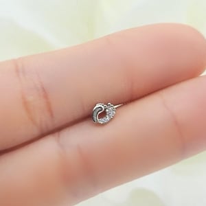 Puede incluir: Un pequeño aro de nariz plateado con un diseño en forma de corazón y piedras de circonita cúbica transparentes.