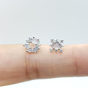 May include: A pair of silver earrings with a pink stone in the center. One earring is a circle with small stones around the edge, and the other earring is a star shape with small stones around the edge.