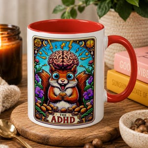 May include: A white ceramic mug with a red interior and handle, featuring a colorful illustration of a squirrel with a brain on its head, surrounded by flowers and nuts, with the text THE ADHD printed at the bottom of the graphic design.