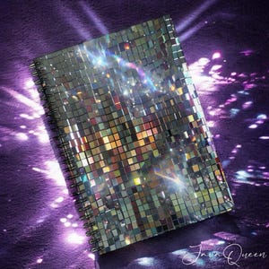 May include: A silver notebook with a mirrored, iridescent cover made of small squares. The notebook has a spiral binding and is lying on a purple surface.