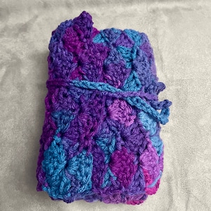 May include: A crocheted blanket in shades of purple and blue, folded and tied with a matching yarn.