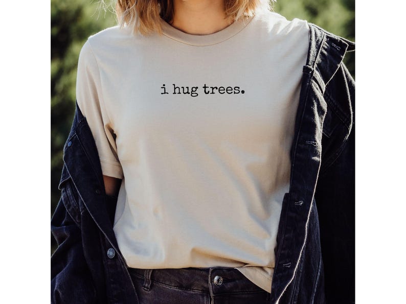 以下が含まれることがあります： 黒い文字で「i hug trees.」とプリントされたベージュのTシャツ