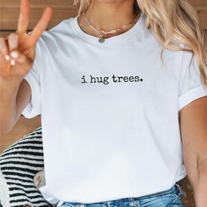 以下が含まれることがあります： 黒い文字で「i hug trees.」とプリントされた白いTシャツです。