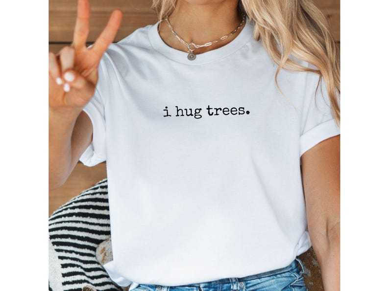以下が含まれることがあります： 黒い文字で「i hug trees.」とプリントされた白いTシャツです。
