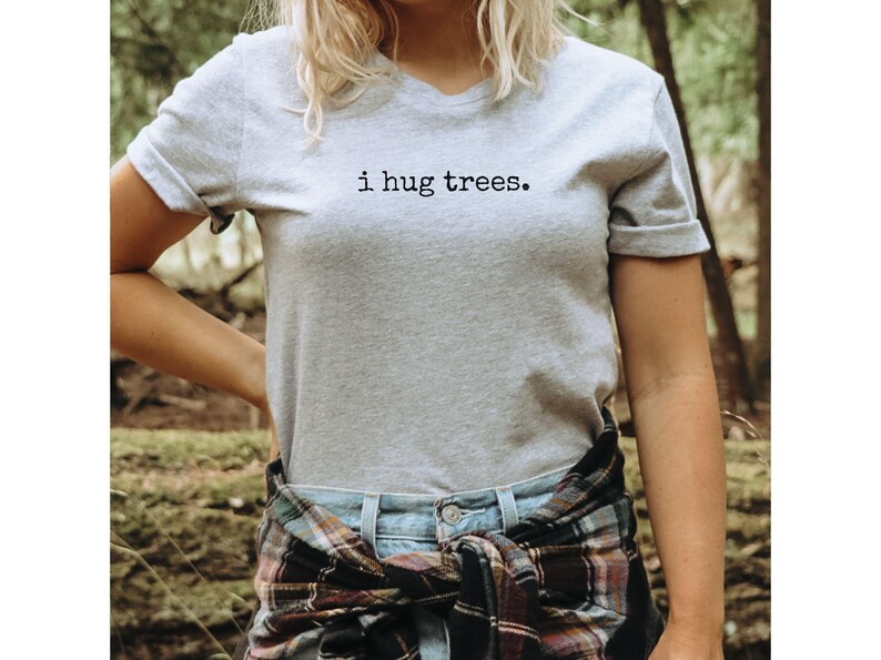 以下が含まれることがあります： VネックのグレーのTシャツで、前面に「i hug trees.」の文字がプリントされています。シャツは、腰にチェック柄のシャツを巻いた人が着ています。