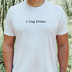 以下が含まれることがあります： 黒い文字で「i hug trees.」とプリントされた白いTシャツ
