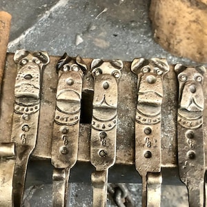 May include: Five metal hooks with dog head designs. The hooks are all the same size and shape, and they are arranged in a row. The hooks are made of a dark metal, and they have a rustic finish.