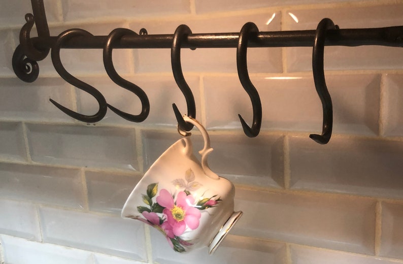 May include: A set of five black metal hooks mounted on a black metal bar. A white teacup with pink floral designs hangs from one of the hooks.