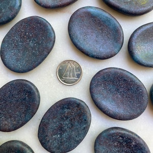 May include: A collection of ten smooth, oval-shaped stones with a dark blue, gray, and brown marbled pattern. The stones are arranged in a semi-circle on a white surface. A Canadian 10-cent coin is in the center of the arrangement.