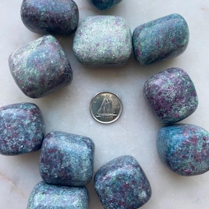 May include: A collection of 11 tumbled green and purple ruby zoisite stones. The stones are smooth and polished, with a variety of shades of green and purple.