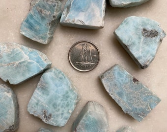 May include: A collection of 12 blue and white polished blue lace agate stones. The stones are various shapes and sizes, and some have a cloudy appearance. A Canadian dime is included for scale.