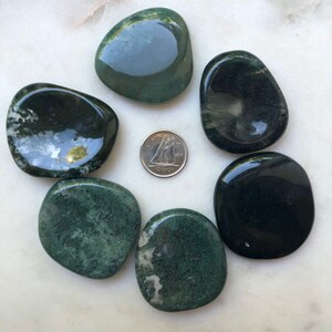 May include: Seven polished green and black agate stones arranged in a circle on a white marble surface. A Canadian 10-cent coin is in the center of the circle.
