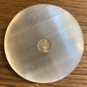 May include: A white selenite charging plate with a Canadian 10-cent coin on top. The coin features a sailboat and the year 2010.