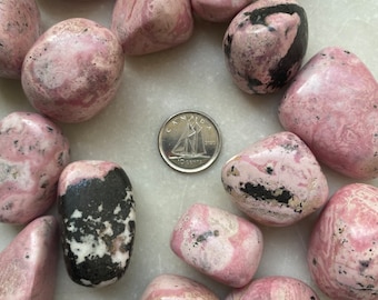 May include: A collection of 14 pink and black tumbled stones. The stones are smooth and have a variety of patterns.