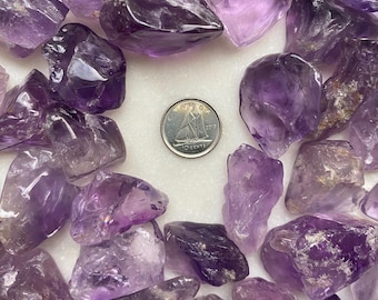 May include: A collection of amethyst crystals in various shapes and sizes. The crystals are a deep purple color and have a natural, rough texture. A Canadian 10-cent coin is included for scale.